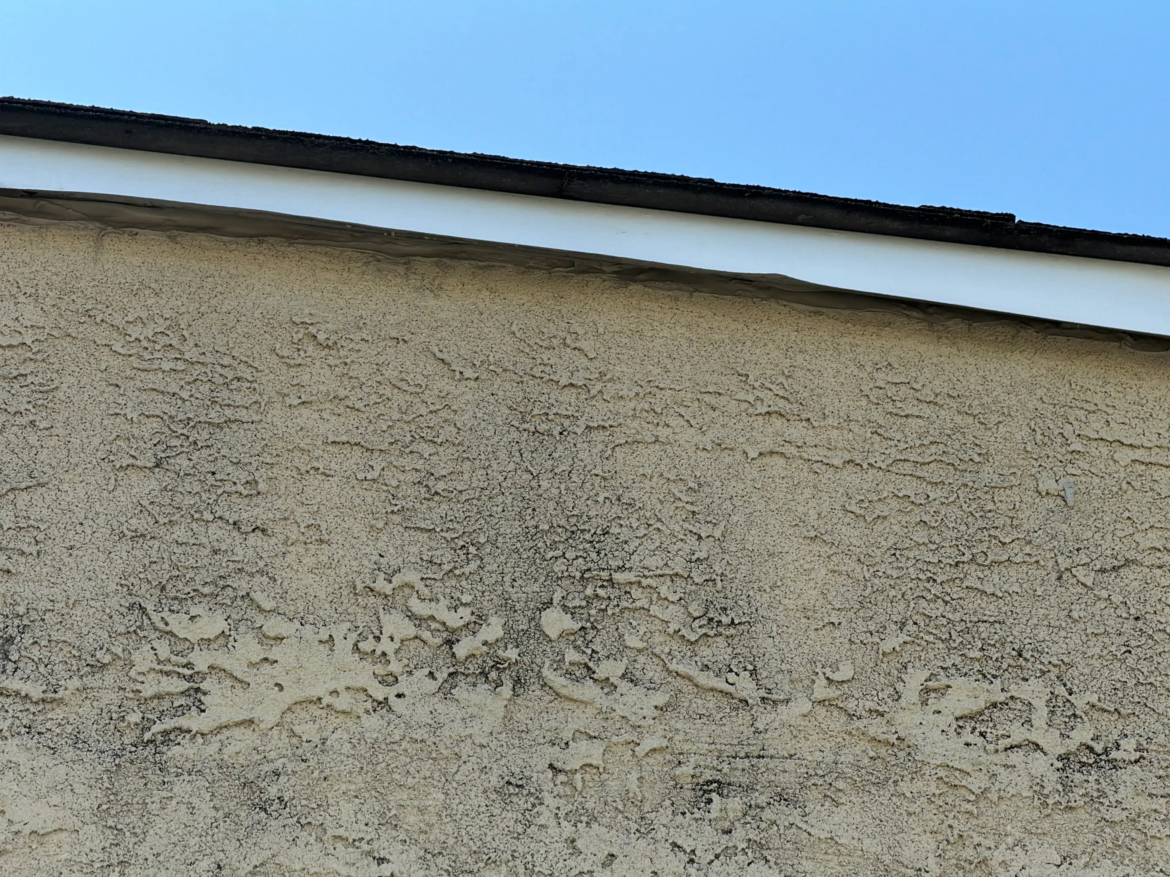 Textured stucco exterior wall painted in tan with white trim and black roof edge