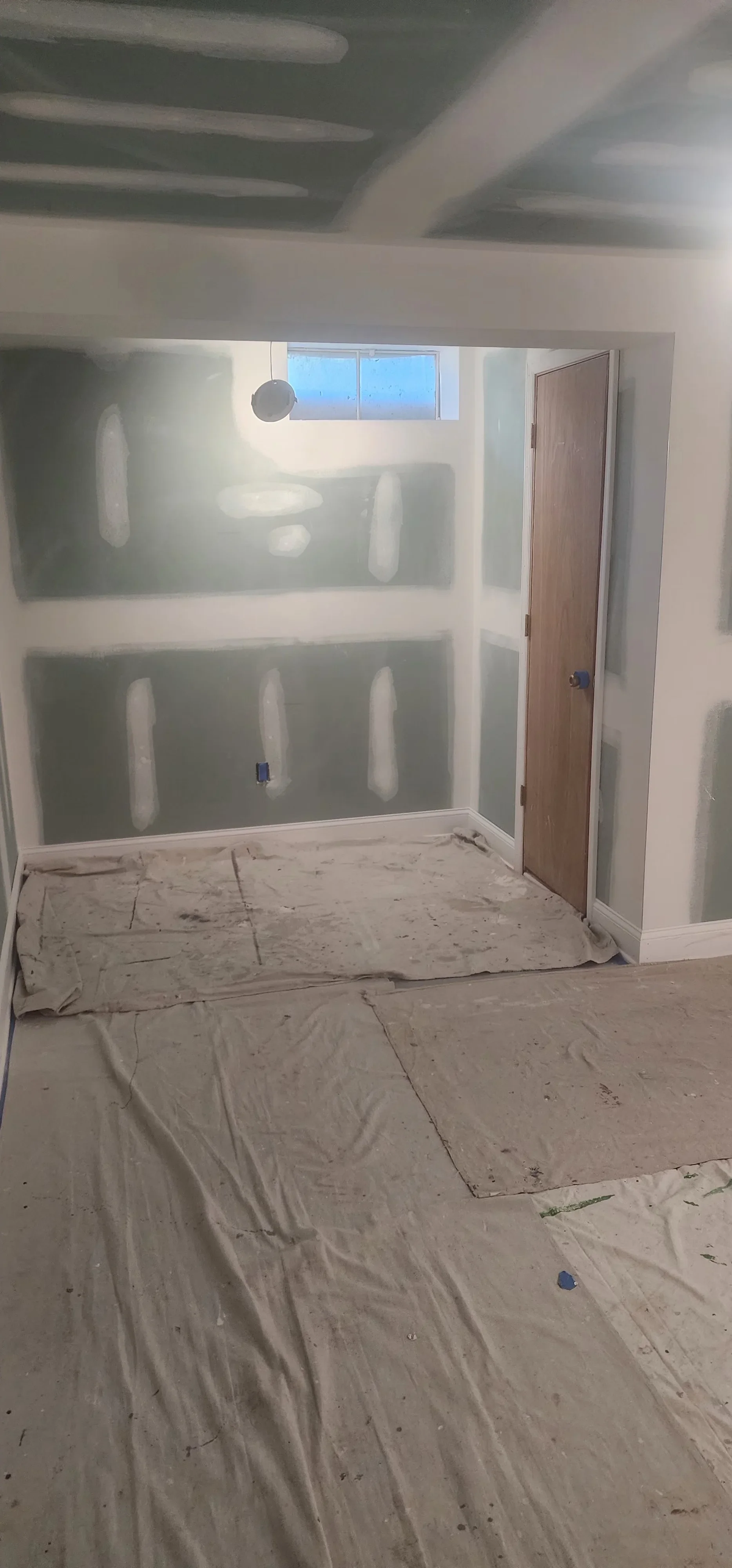 Drywall-taped interior room with finished walls and protective floor coverings
