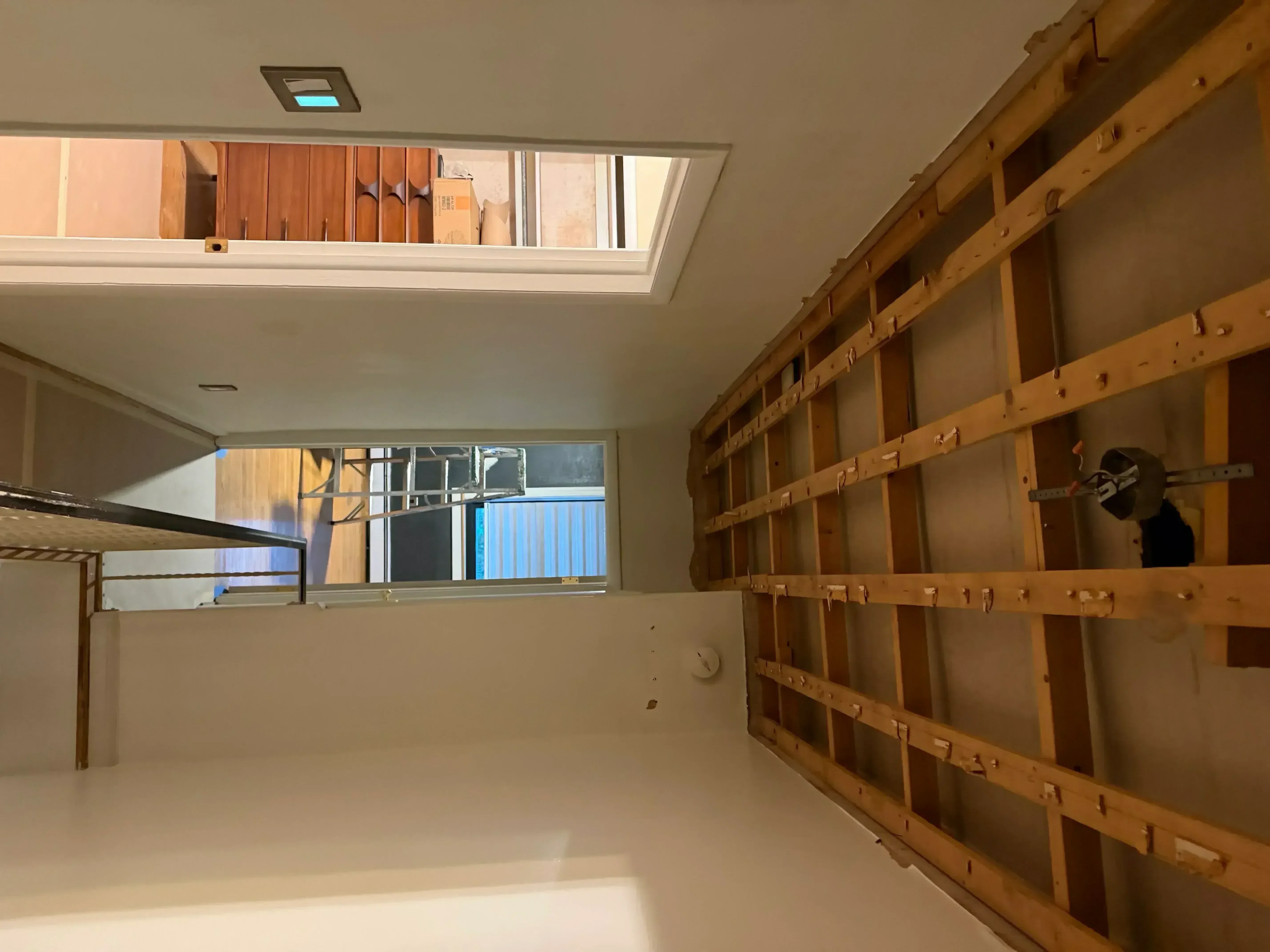 Drywall installation with wooden framing studs, recessed lighting, and window openings in interior space
