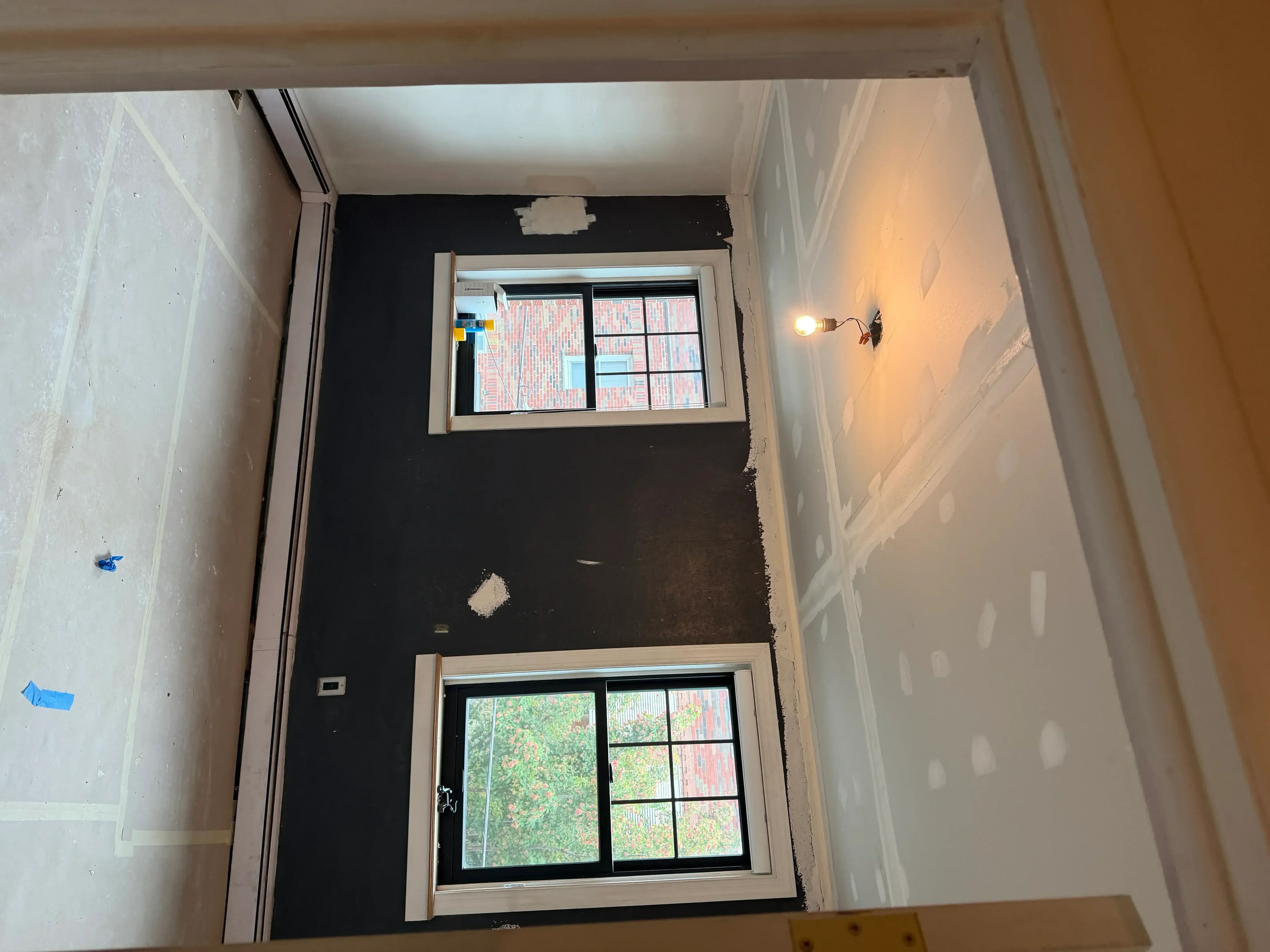 Interior drywall with black primer, white trim windows, and compound patches ready for painting