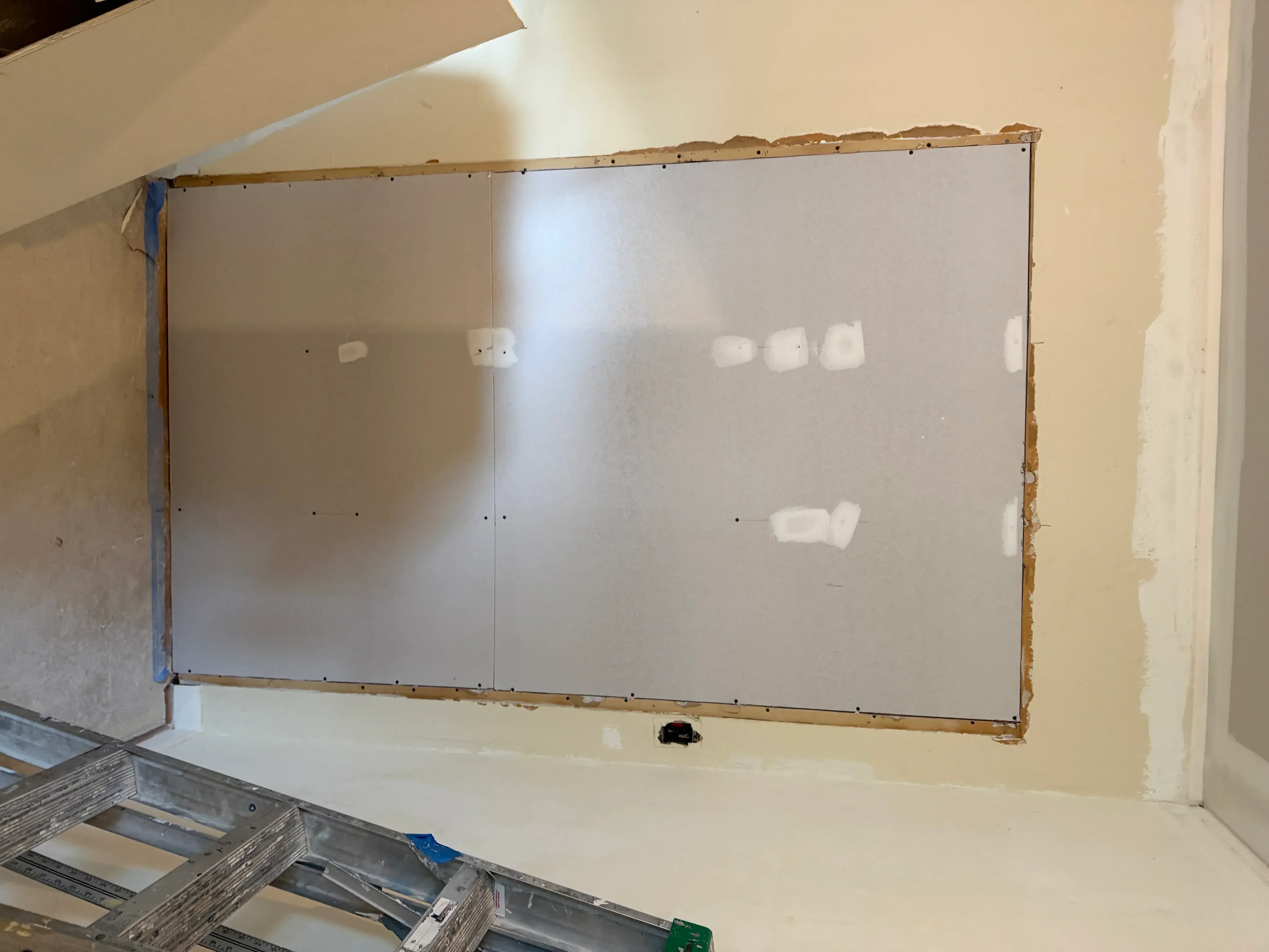 Drywall sheets with taped seams and joint compound applied, metal stud framing visible