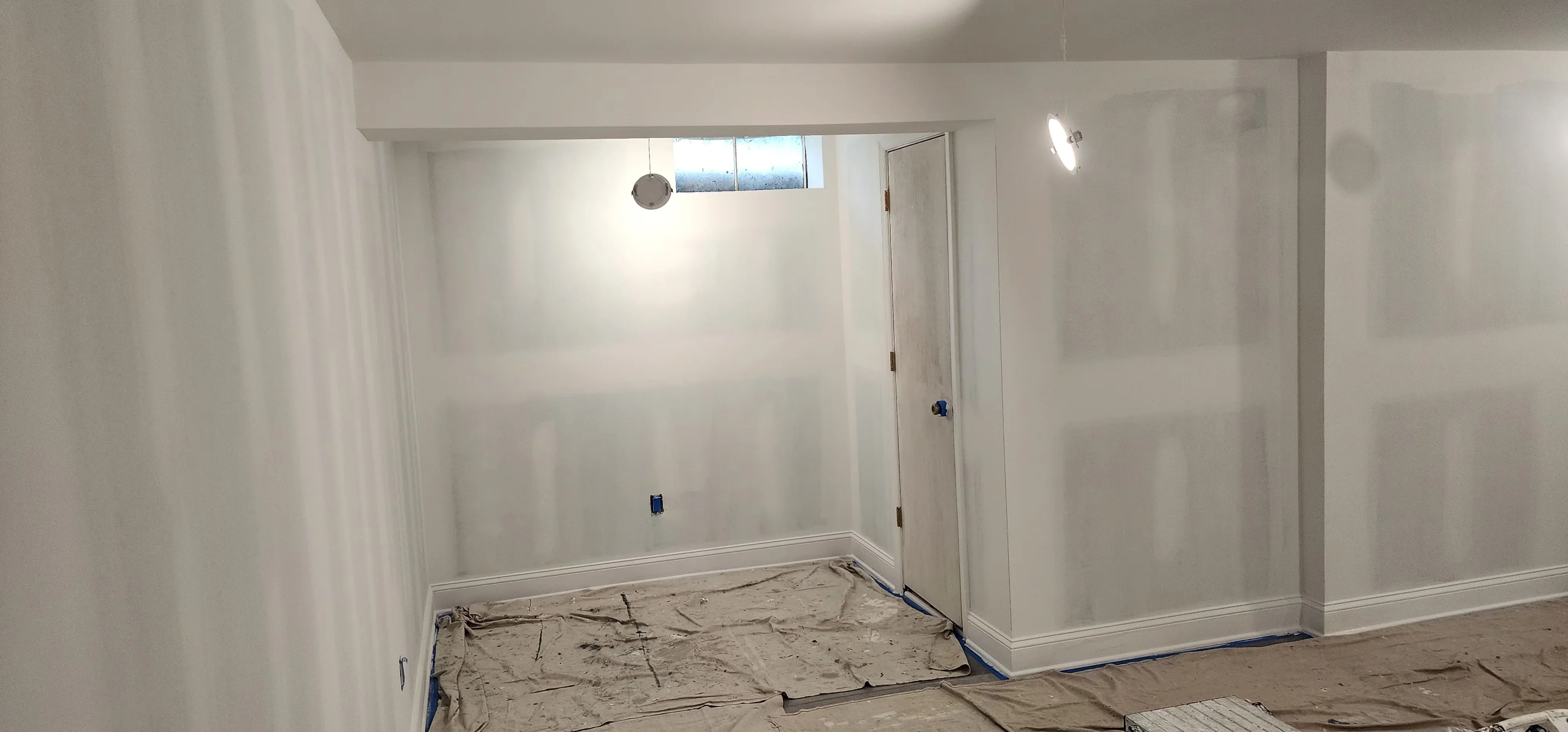 Freshly finished drywall with smooth walls, white primer coat, and taped seams ready for painting