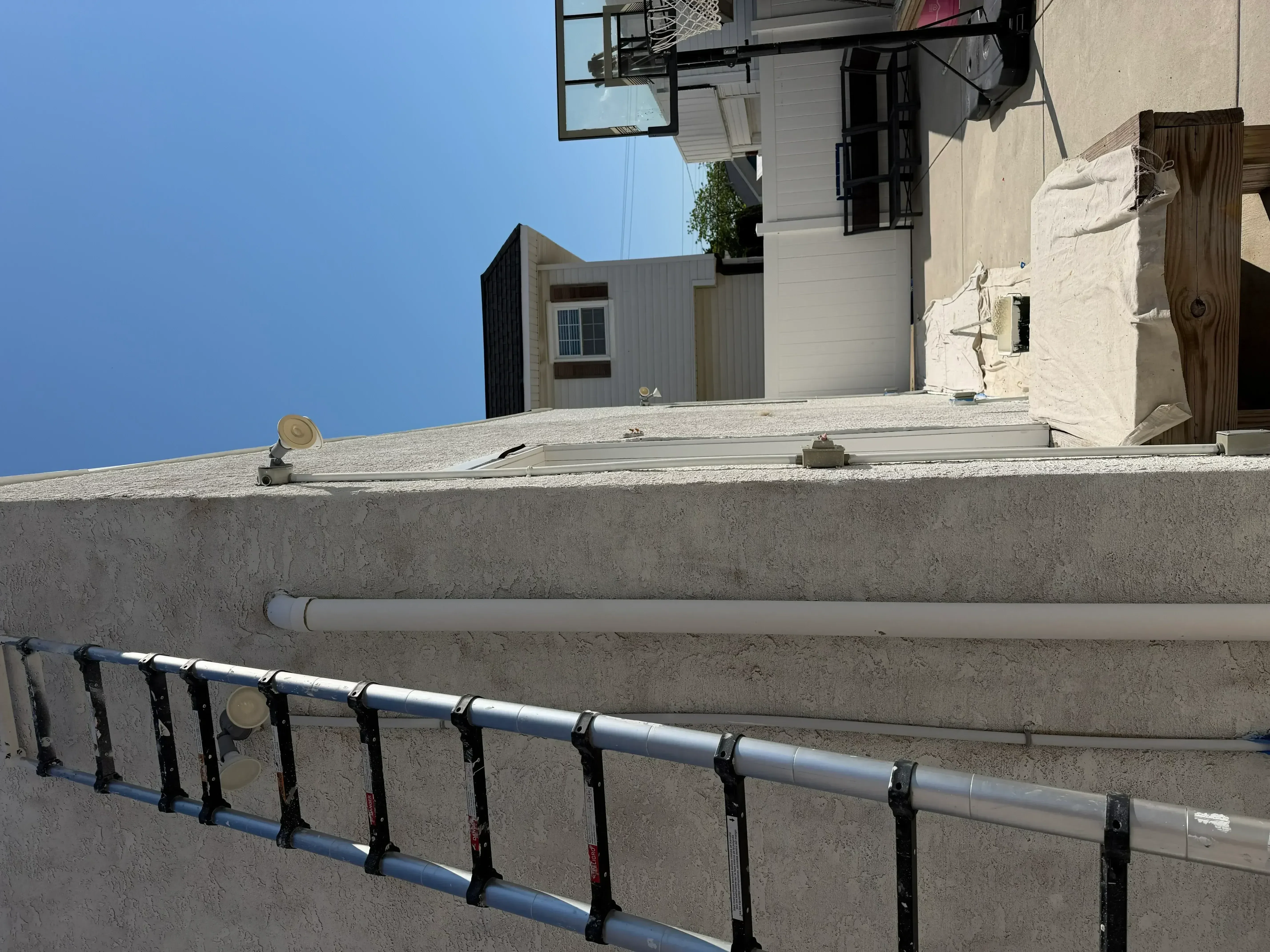Concrete flat roof with gray protective coating, metal drainage pipe, and black safety railing system