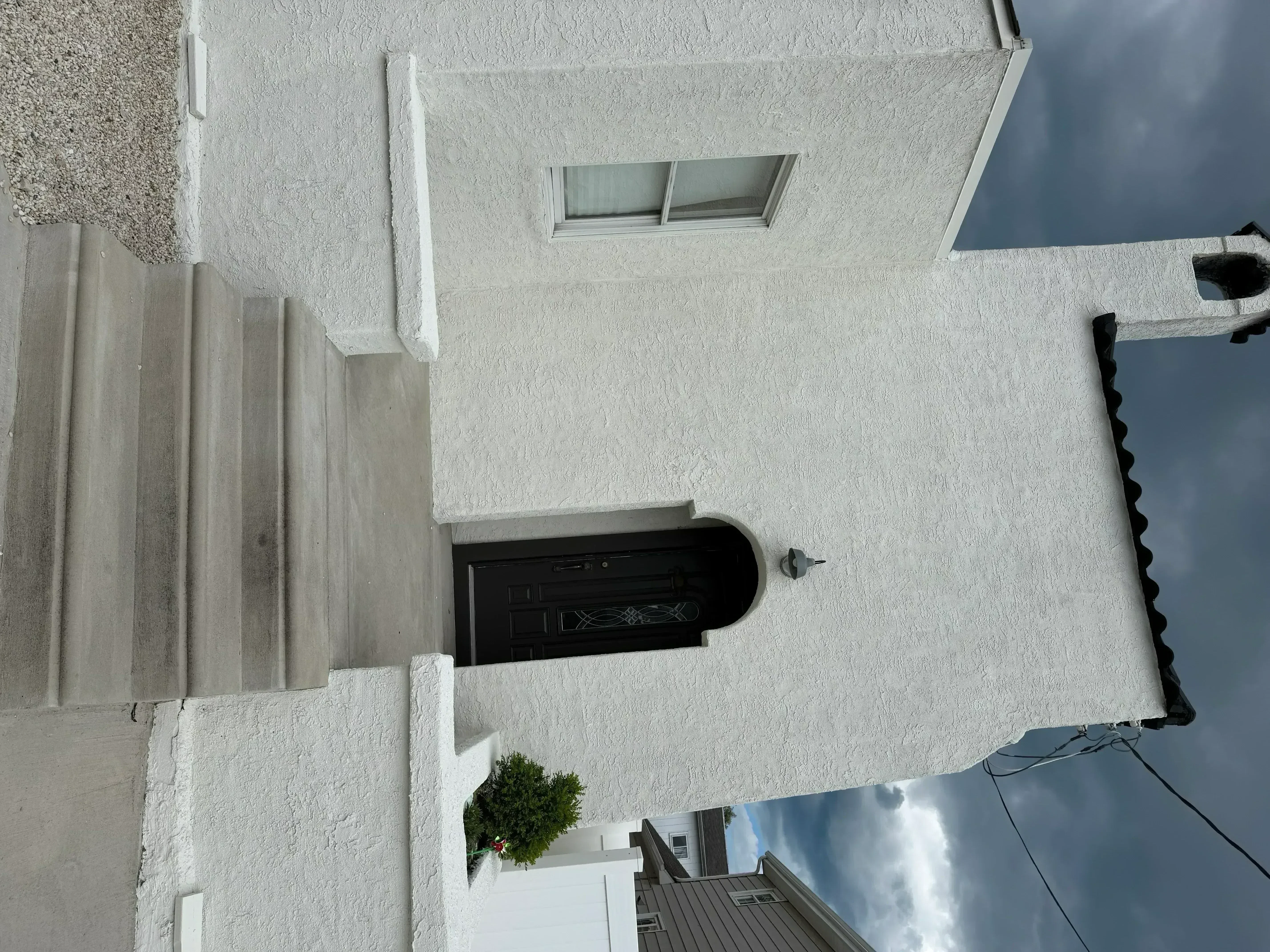 White stucco exterior wall with black entry door, window, and concrete fence panels