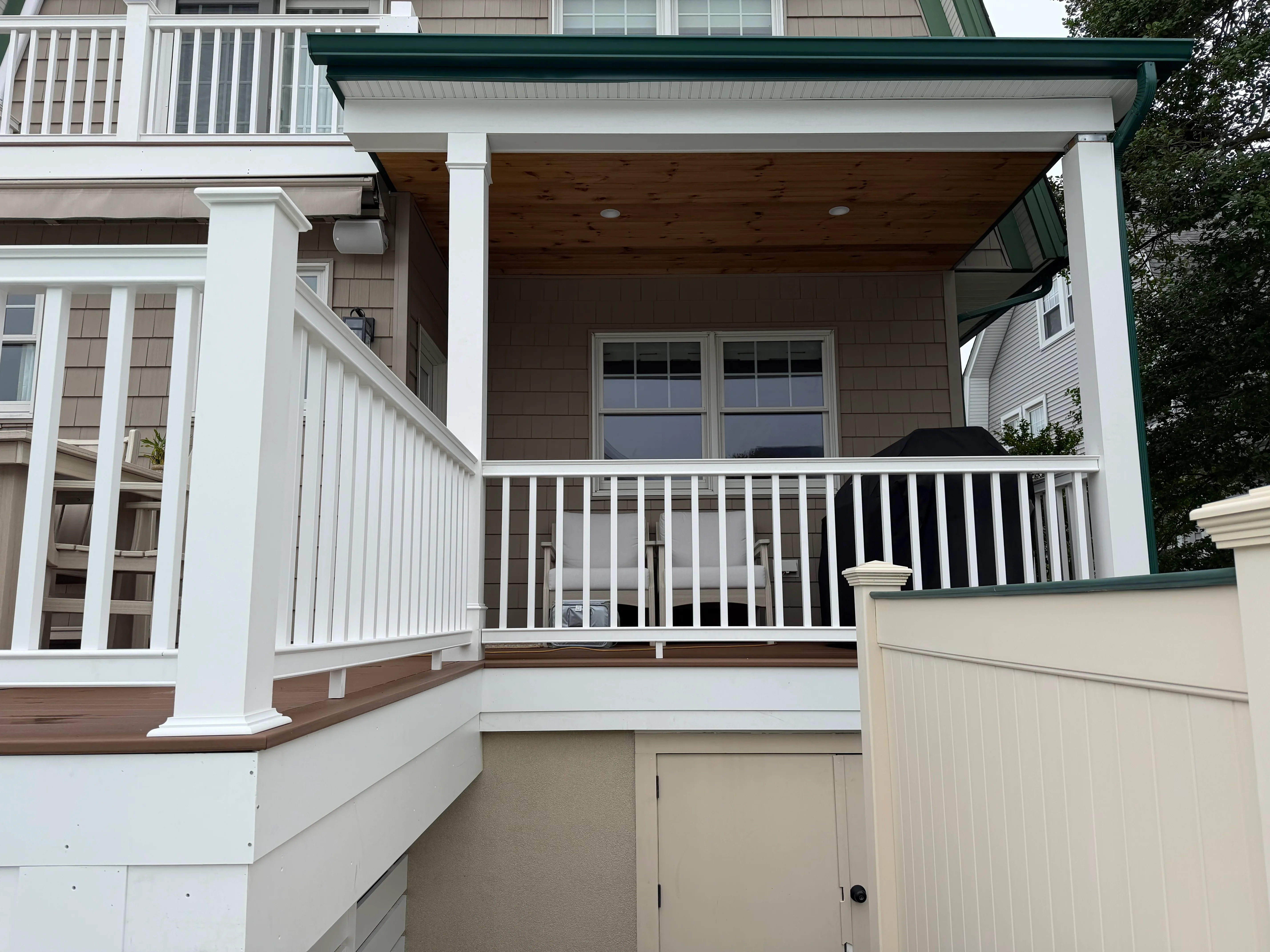 White-trimmed deck with dark green roof, stained wood ceiling, and white railings on multi-level residential addition
