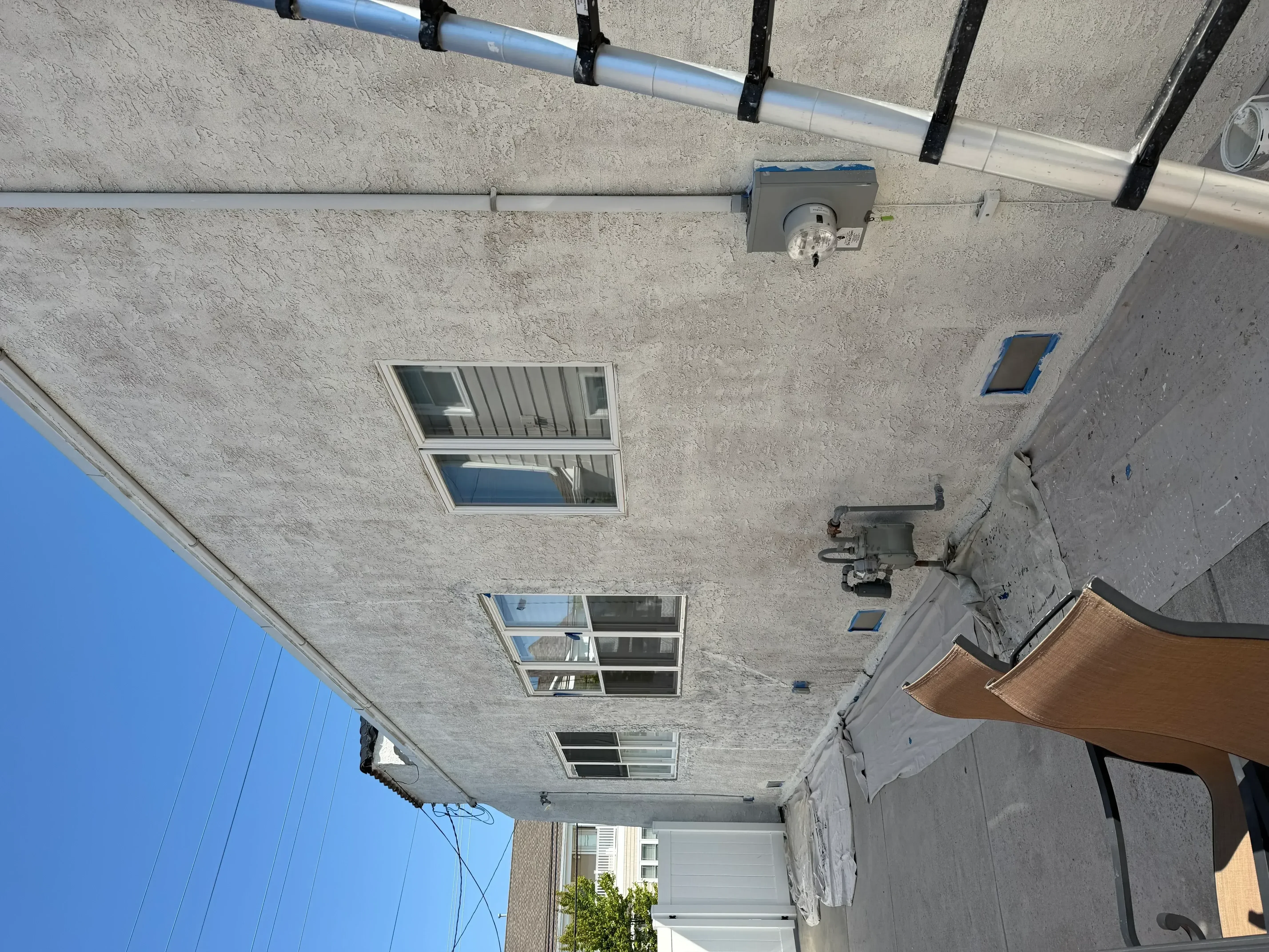Painted concrete exterior wall with windows, electrical outlet, and metal conduit installation