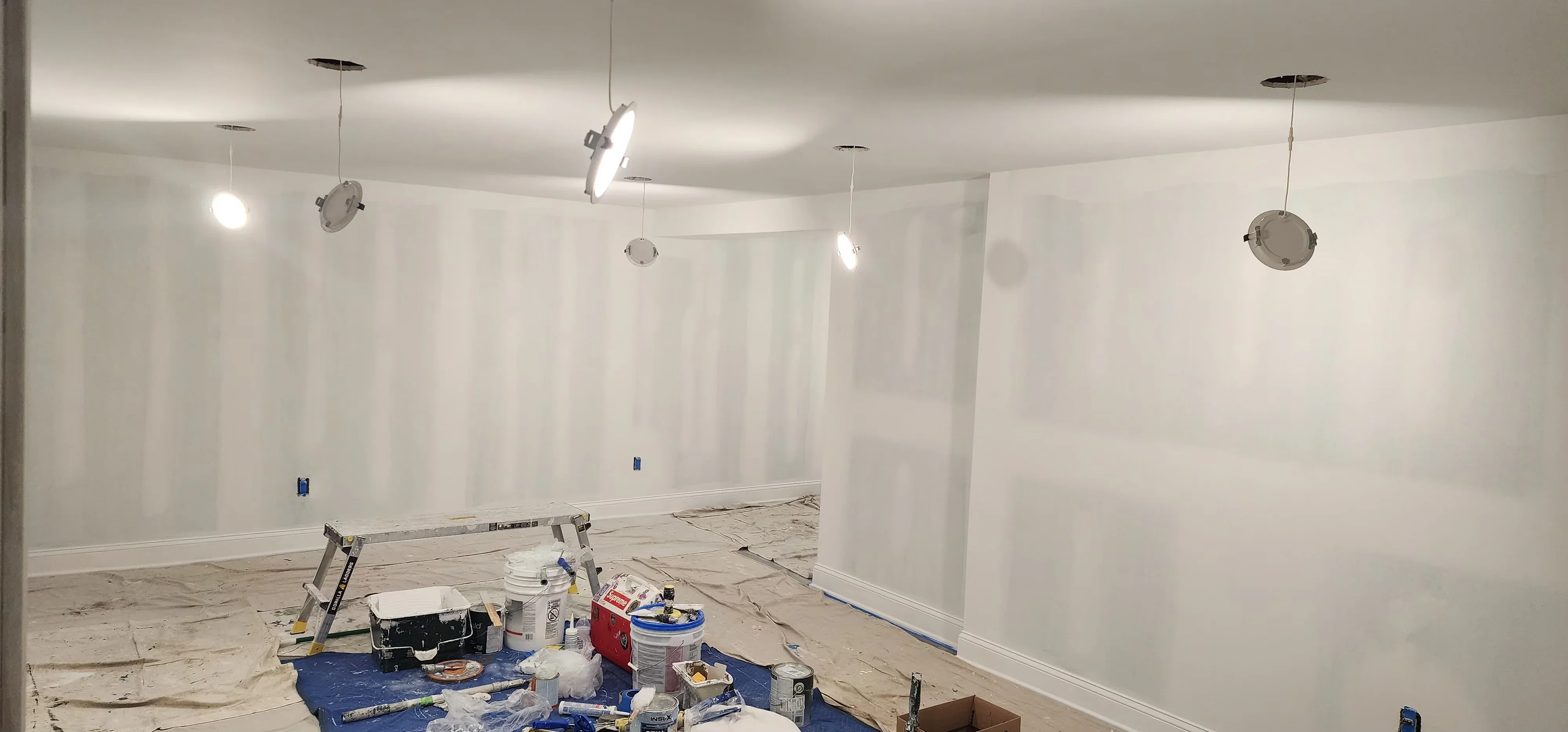 Commercial interior with drywall installation, taped seams, pendant lights, and recessed fixtures ready for painting