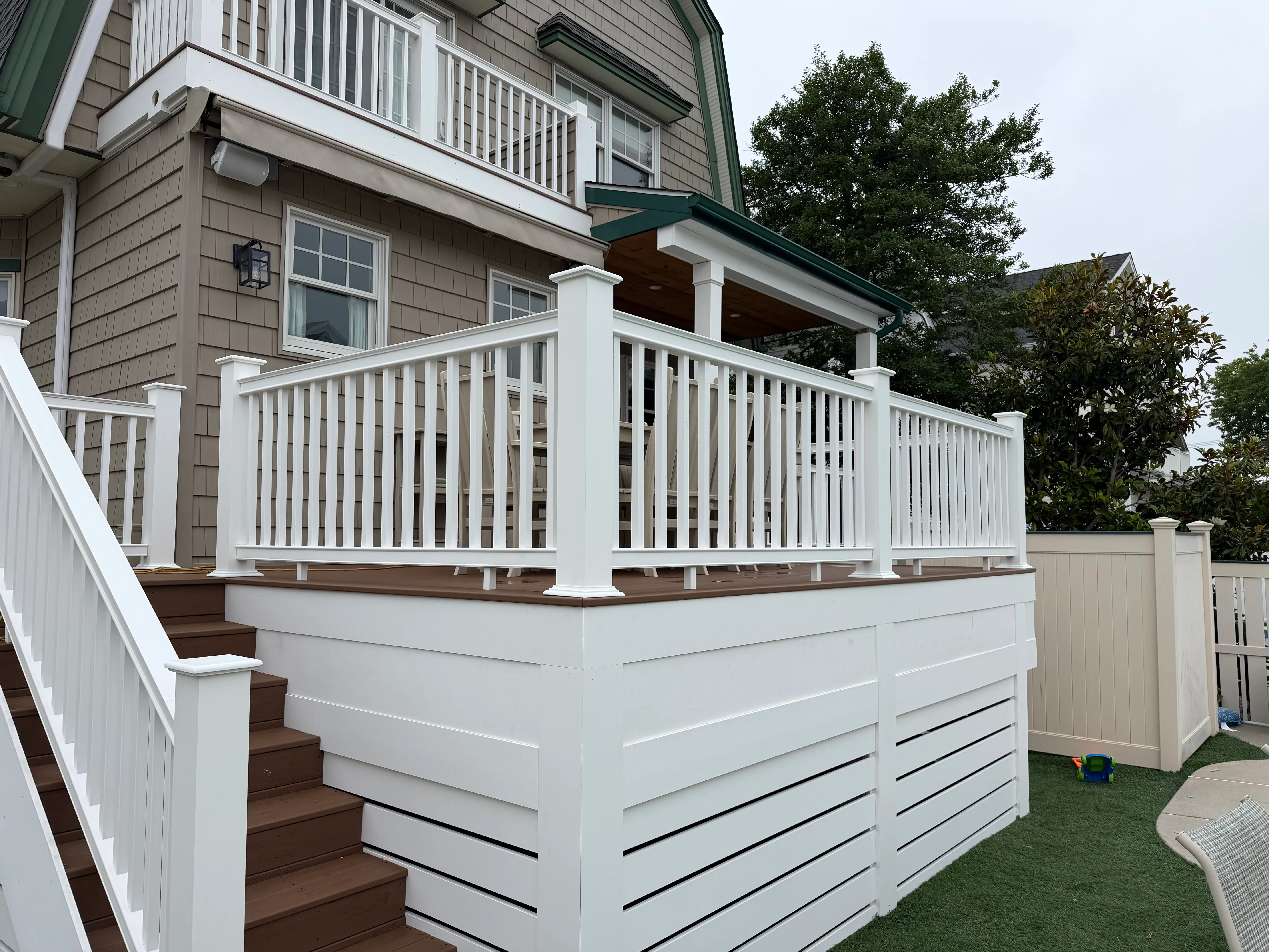 White painted deck railings, posts, and skirting with brown composite decking and covered porch overhead
