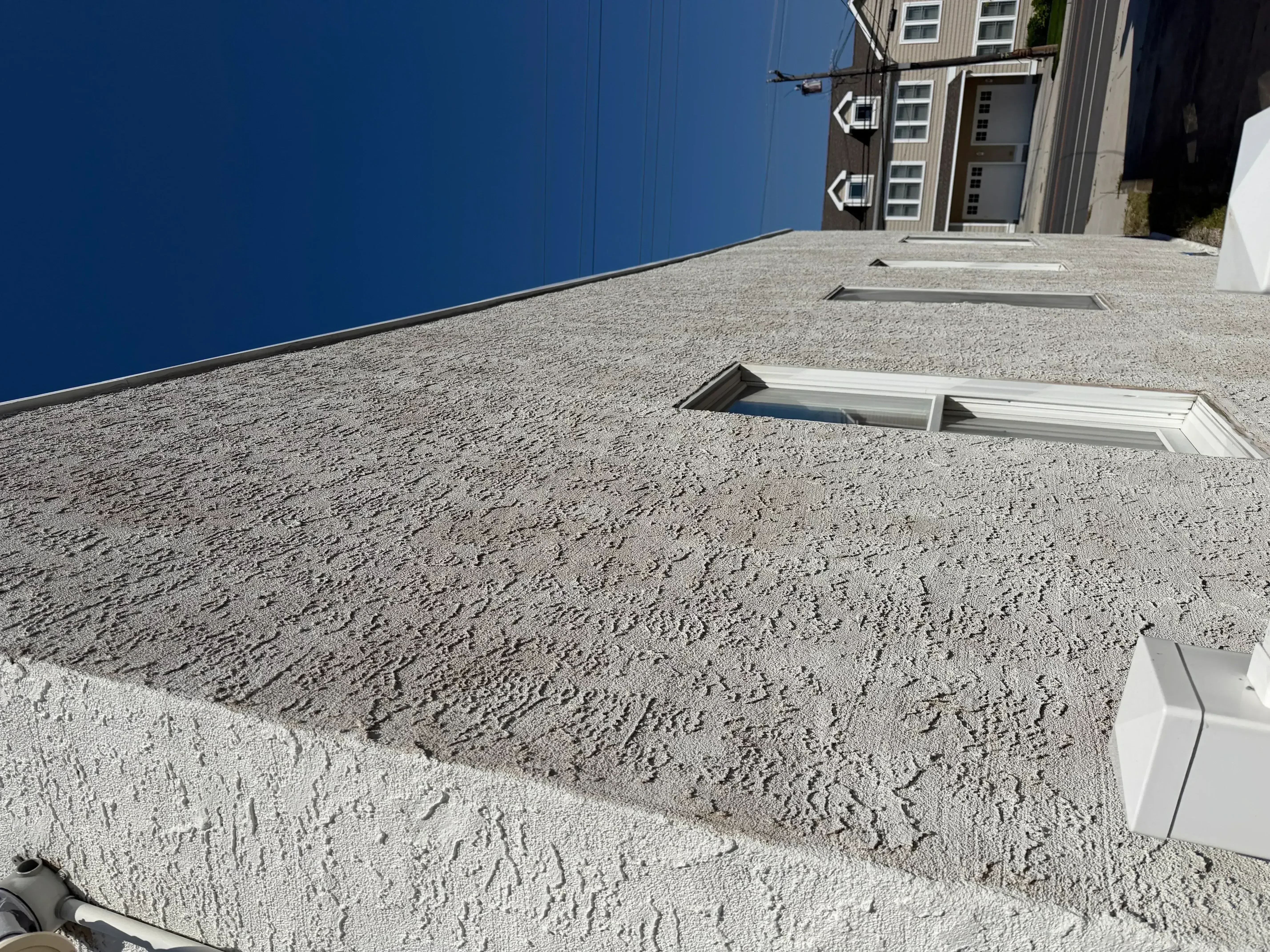Gray textured roof coating with white flashing and penetration boots on flat commercial roof