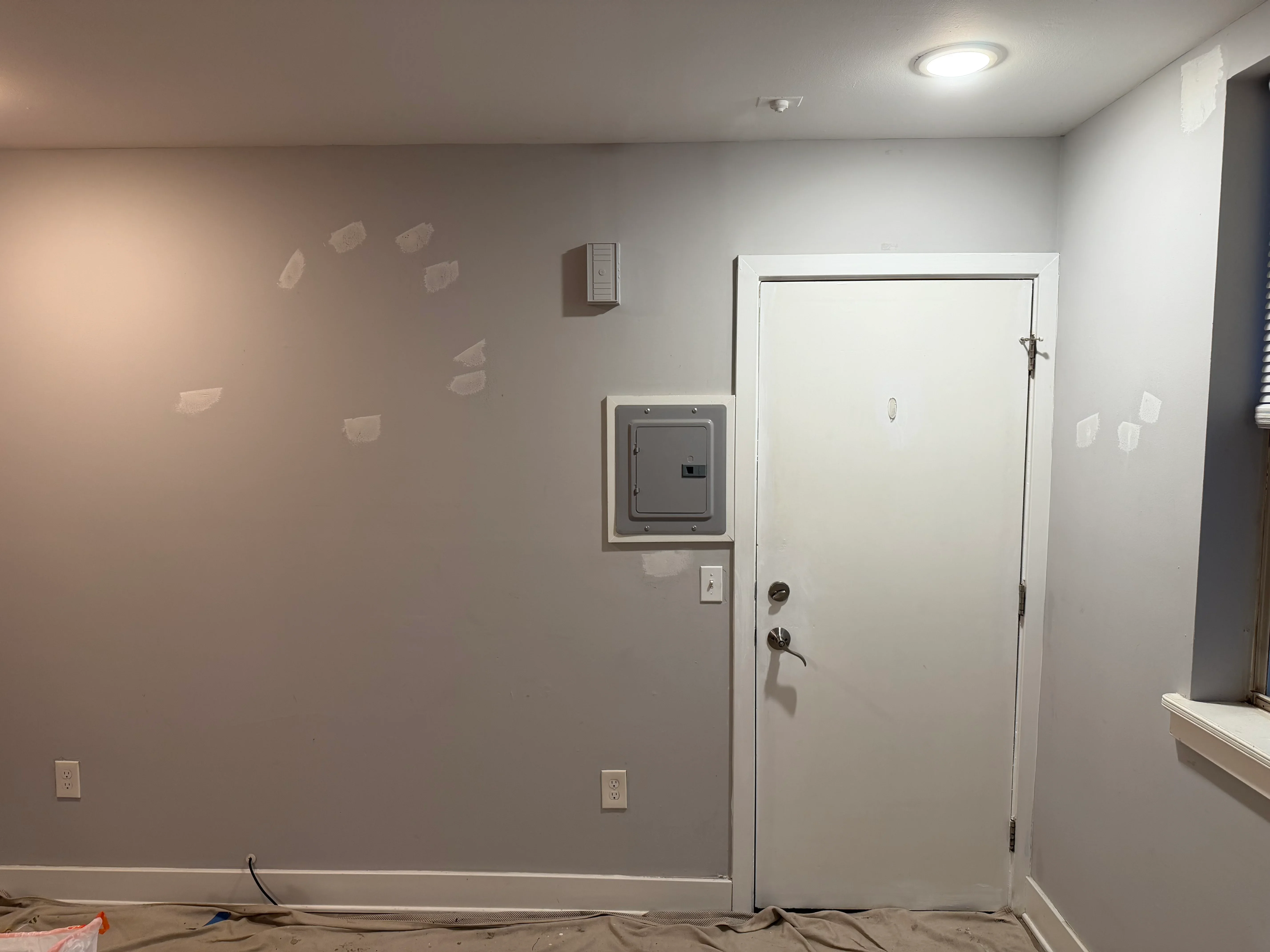 Drywall patches and primer on interior walls with electrical outlets and white door frame