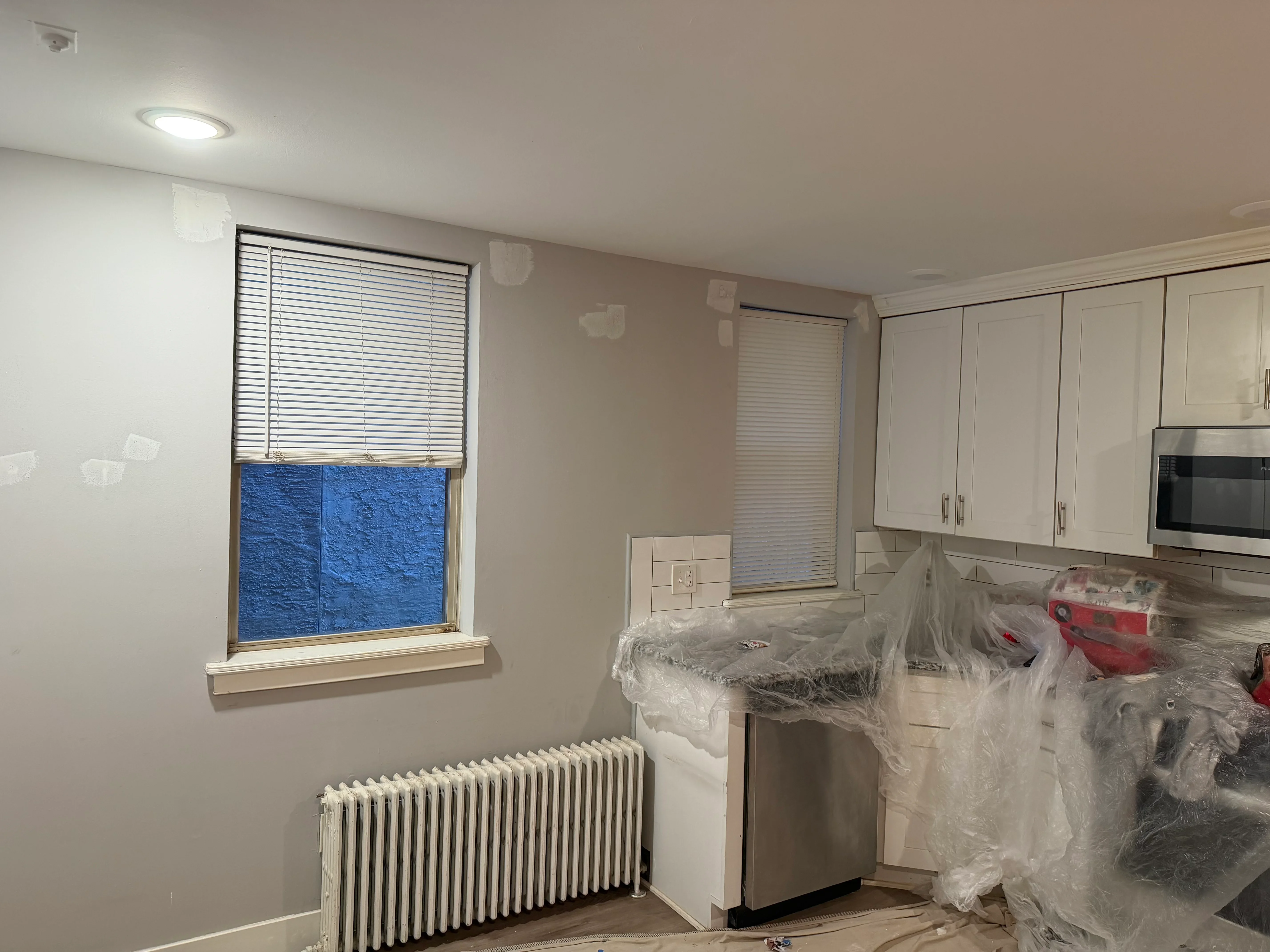 Kitchen with freshly painted walls, drywall patches, recessed lighting, and protective coverings on cabinets