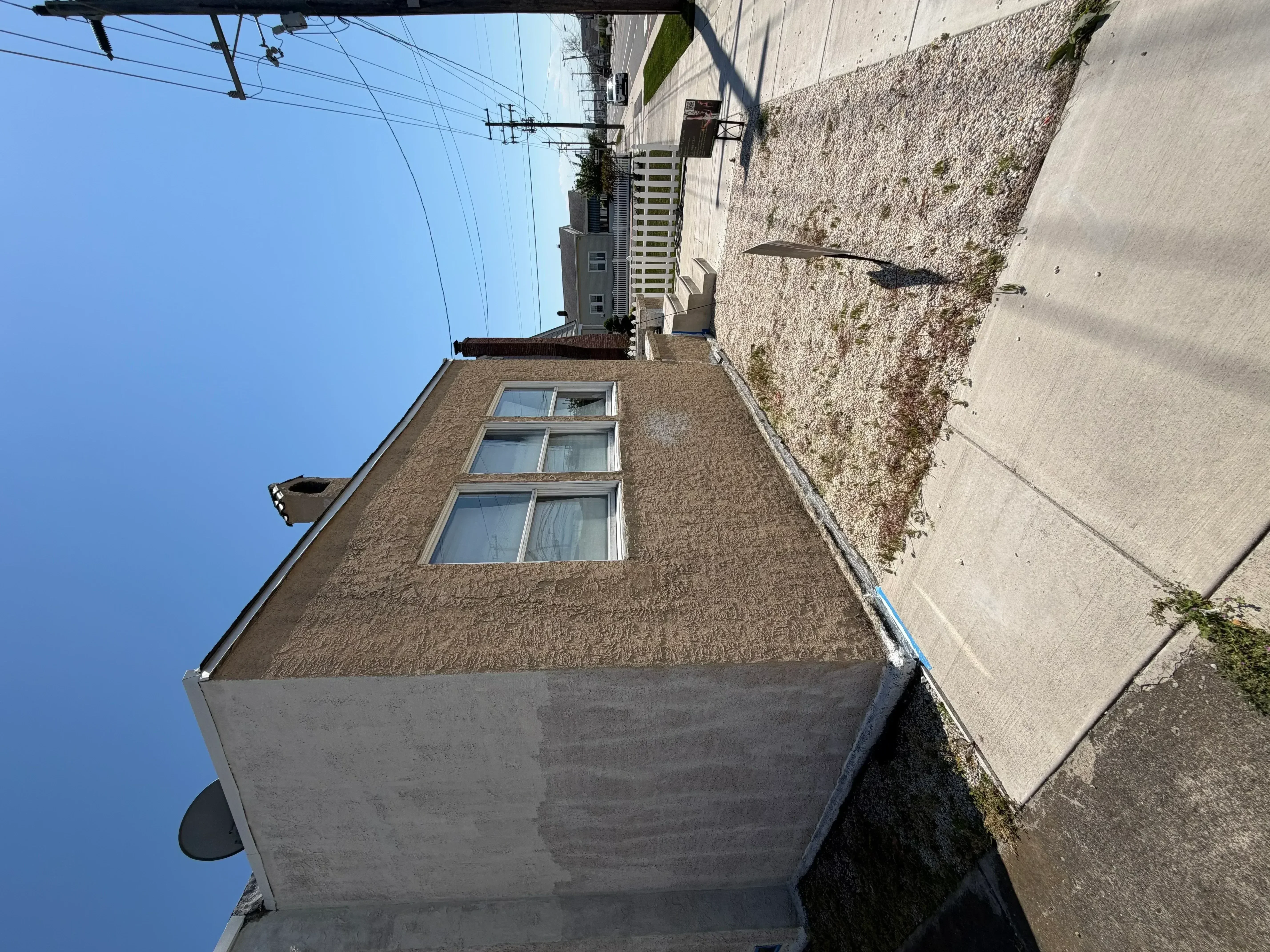 Exterior house painting with tan textured finish and white-trimmed windows
