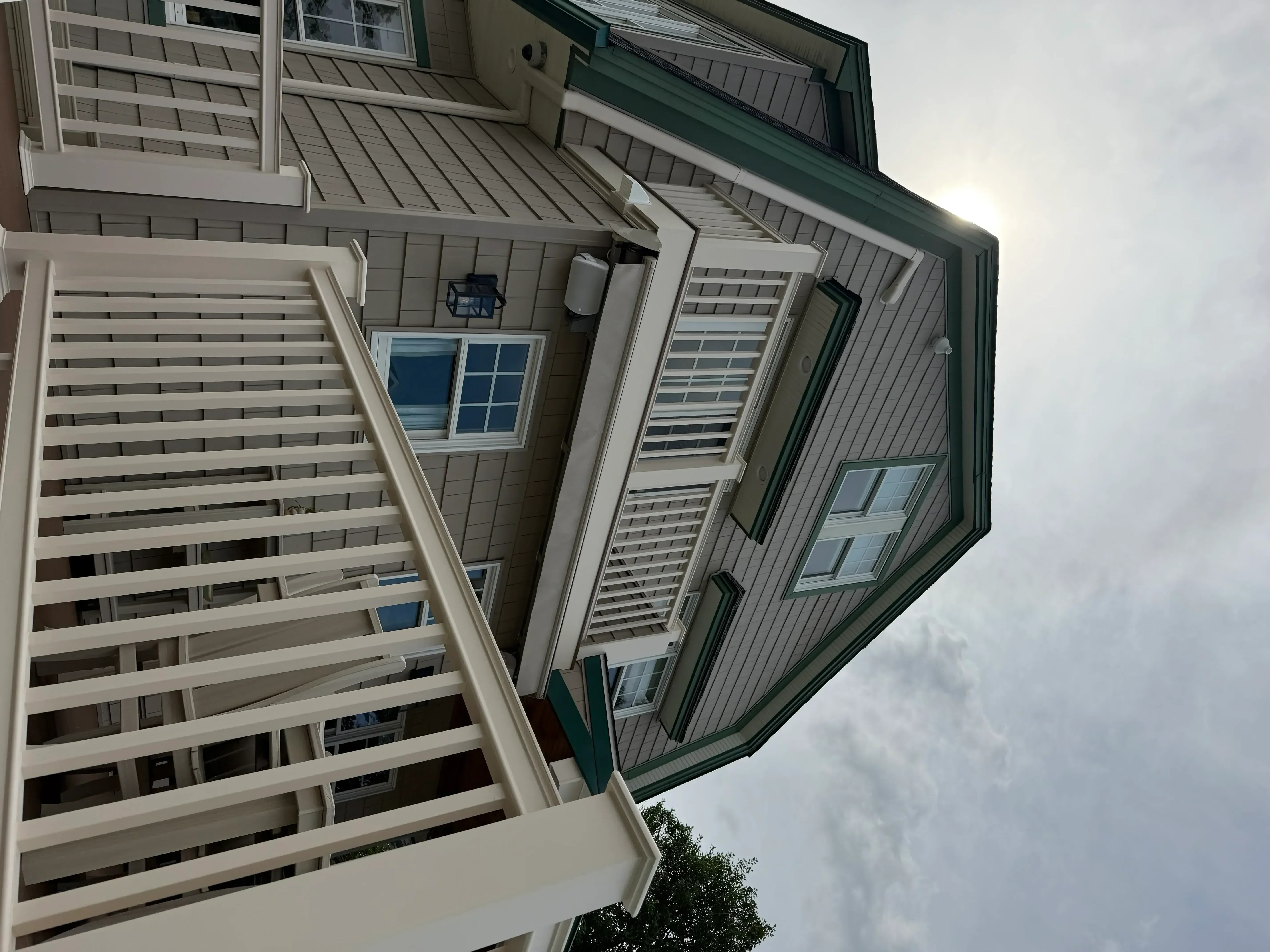 Gray metal siding with dark green trim, white painted windows, shutters, and deck railings on residential home