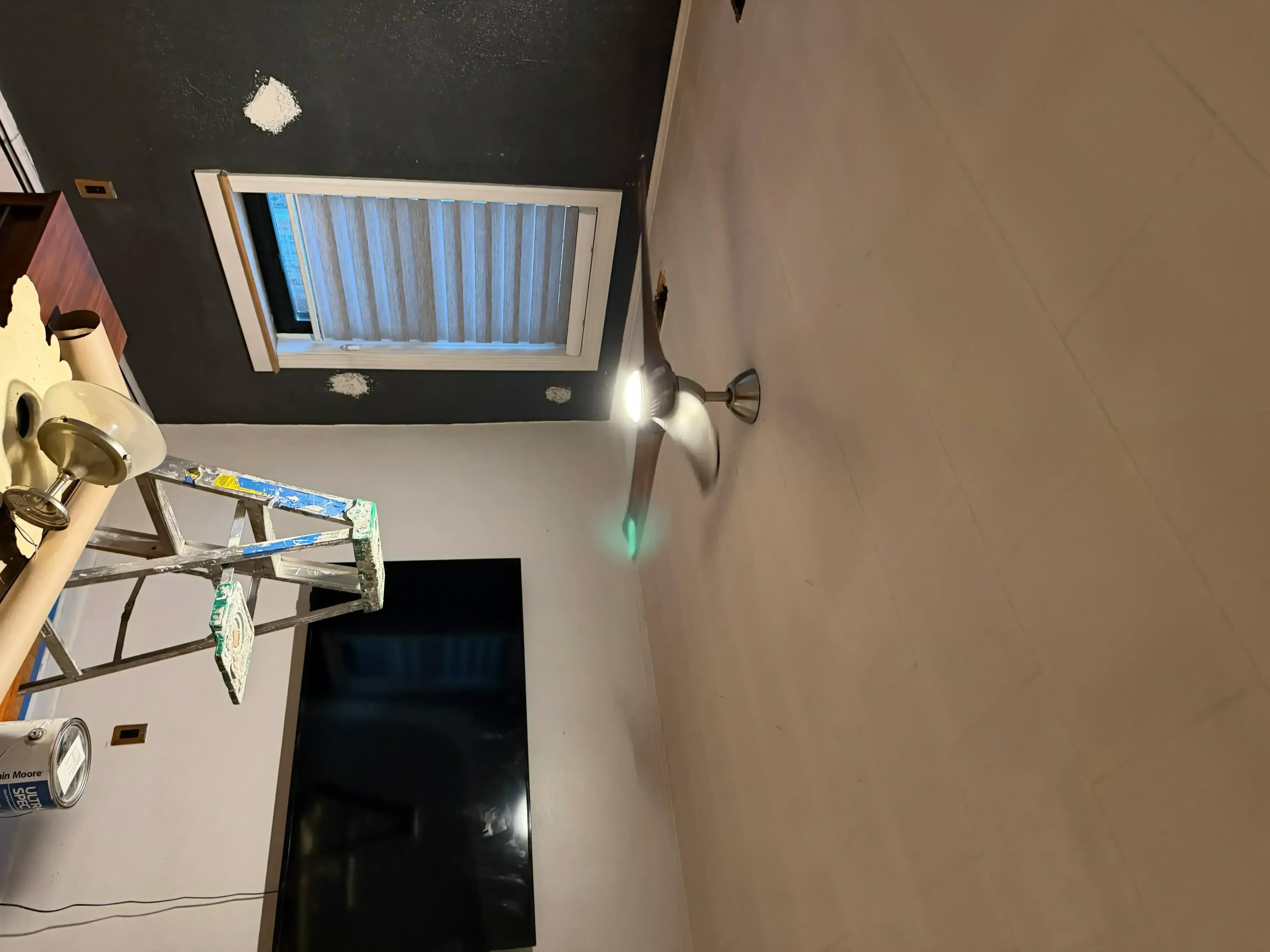 Interior room with freshly painted drywall walls and white trim, work in progress with protective coverings and painting equipment